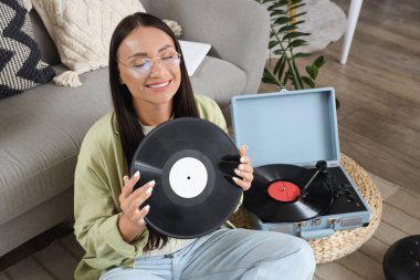 Plak çalar için vinil diski olan genç bir kadın evde oturuyor.