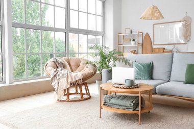 Pencerenin yanındaki sehpanın üzerinde gri kanepe ve modern dizüstü bilgisayarla aydınlık oturma odasının içinde.