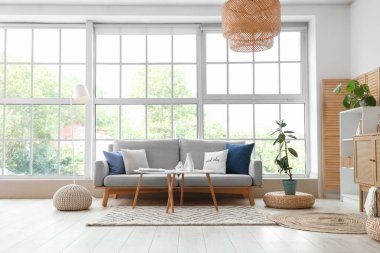 Pencerenin yanında gri kanepesi ve sehpası olan modern oturma odasının içinde.