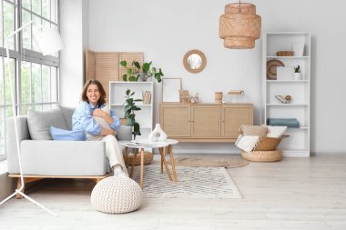 Gri kanepede oturan güzel genç bayan. Açık oturma odasındaki pencerenin yanında.