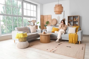 Gri kanepede oturan çay bardağıyla güzel, genç bir kadın.