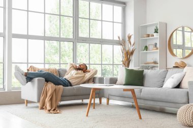 Genç adam evdeki rahat kanepede dinleniyor.