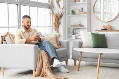 Evdeki rahat koltukta cep telefonuyla sohbet eden genç adam.