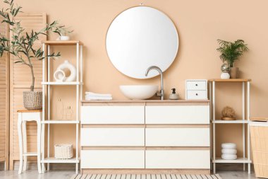 Lavabosu, çekmecesi ve bej duvarın yanında raf ünitesi olan şık bir banyo.