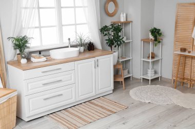 Lavabosu, çekmecesi ve pencerenin yanındaki raf üniteleri olan şık bir banyo.