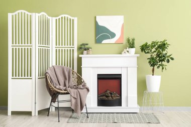 Beyaz şömine, ev bitkileri, koltuk ve katlanır perde şık oturma odasının içinde.