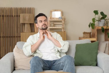 Yakışıklı adam evdeki kanepede tiroit bezini inceliyor.