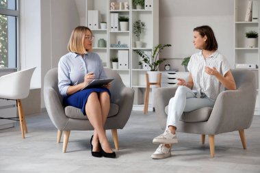 Ofisteki koltuklarda oturan genç kızı dinleyen kadın psikolog.