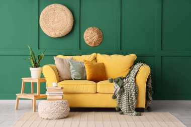 Yeşil duvarın yanında rahat sarı kanepesi olan şık bir oda.