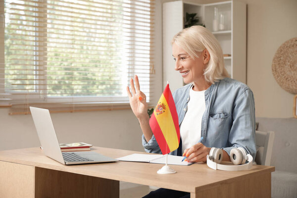Mature woman with flag of Spain learning language online at table