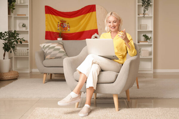 Mature woman with laptop learning Spanish online in armchair at home