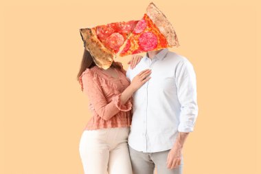 Bej arka planda başlarını kucaklamak yerine pizza dilimleri olan mutlu genç bir çift.