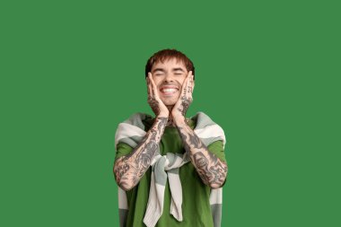 Yeşil arka plandaki yakışıklı, gülümseyen genç adam.