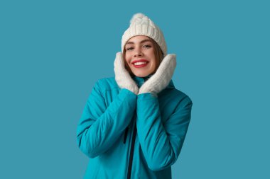Mavi arka planda sıcak kış giysileri içinde güzel, genç, mutlu bir kadın.