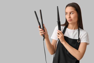 Saç maşasıyla kadın kuaför ve gri arka planda ütü düzleştirici.