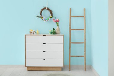 Güzel Paskalya çelengi mavi duvarda yumurtalarla süslenmiş. Odadaki çekmecelerin yanında.