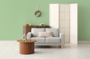 Yeşil duvarda güzel Paskalya çelengi ve şık oturma odasında rahat bir kanepe.