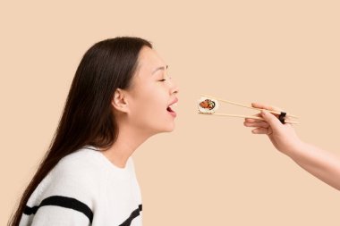 Güzel genç Asyalı kadın ve kadın eli bej arka planda lezzetli suşi rulosu.