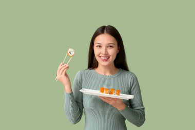 Güzel, Asyalı bir kadın elinde çubuk ve lezzetli suşi tabağıyla yeşil arka planda yuvarlanıyor.