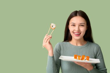 Güzel, Asyalı bir kadın elinde çubuk ve lezzetli suşi tabağıyla yeşil arka planda yuvarlanıyor.