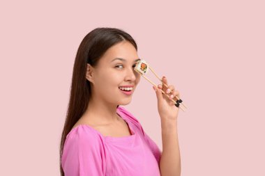 Güzel genç Asyalı bir kadın bir gözünü lezzetli suşilerle kaplıyor soluk pembe arka planda suşi yuvarlanıyor.