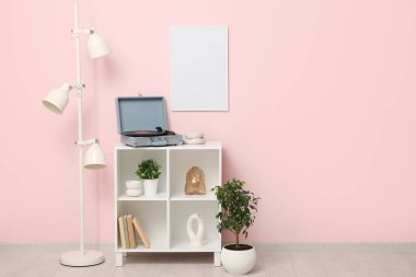 Pembe duvarın yanındaki raf ünitesinde disk ve ev dekorasyonuna sahip kayıt çalar