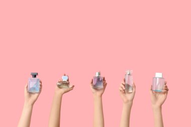 Pembe arka planda bir sürü parfüm şişesi olan kadın elleri.