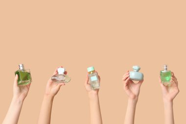 Kahverengi arka planda bir sürü parfüm şişesi olan kadın elleri.