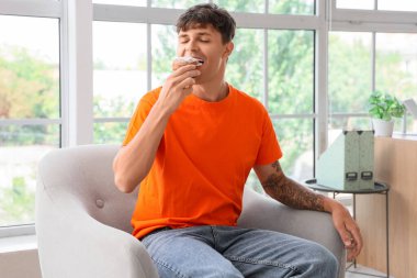 Genç adam evdeki koltukta lezzetli çörekler yiyor.