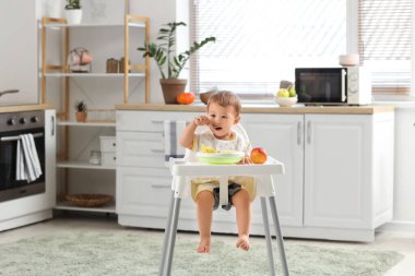 Tatlı küçük bebek lezzetli meyveler yiyor ve evdeki mutfakta sandalyede oturuyor.