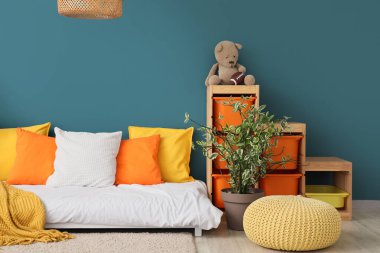 Rahat yatak, ev bitkisi ve raflar çocuk odasındaki renkli duvarın yanında oyuncaklar.