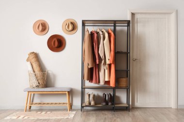 Gri banklı, şapkalı ve sonbahar kıyafetleri askıda asılı şık bir soyunma odası.