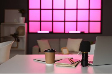 Podcaster 'ın stüdyosundaki sehpanın üzerinde not defterleri ve kahve fincanı olan mikrofon.