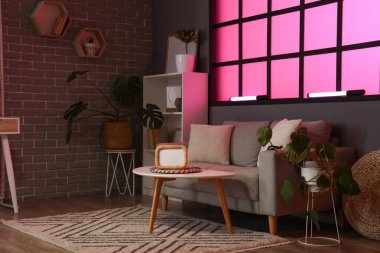 Karanlık podcaster stüdyosunun içinde kanepe, masa ve raf ünitesi var.