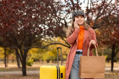 Sonbahar günü çantalı kadın turist parkta cep telefonuyla konuşuyor.
