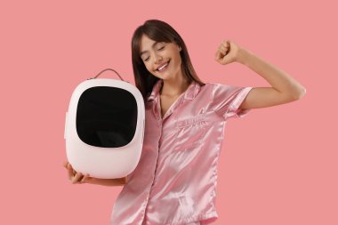 Pembe arka planda kozmetik ürünleri için küçük buzdolabı olan güzel genç bir kadın.