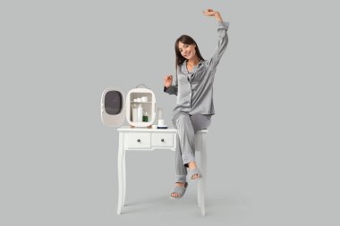 Gri arka planda kozmetik ürünleri için küçük buzdolabı olan güzel genç bir kadın.