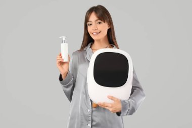 Gri arka planda kozmetik ürünleri için küçük buzdolabı olan güzel genç bir kadın.