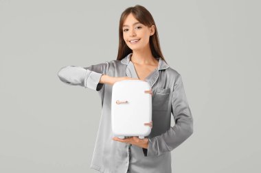 Gri arka planda kozmetik ürünleri için küçük buzdolabı olan güzel genç bir kadın.