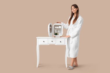 Bej arka planda kozmetik ürünleri için küçük buzdolabı olan güzel genç bir kadın.