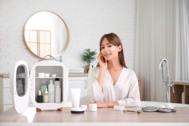 Küçük buzdolabı ve kozmetik ürünleriyle banyoda güzel bir genç kadın.