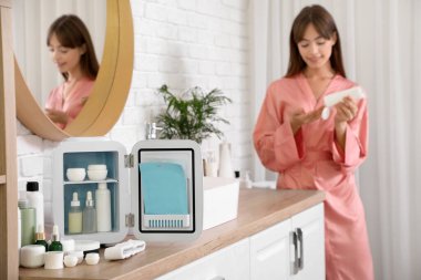 Banyoda kozmetik ürünleri ve küçük buzdolabı olan güzel genç bir kadın.