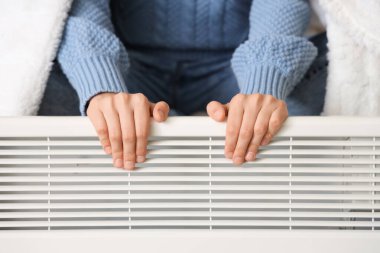 Yatak odasında elektrikli ısıtıcısı olan genç bir kadın, yakın plan.