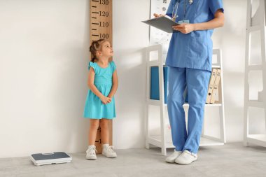 Klinikte stadyum ölçeri yakınında boyunu ölçen küçük tatlı bir kızı olan bir çocuk doktoru.