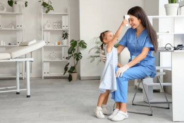 Klinikte çocuk doktorunun ateşini ölçen kızıl ötesi termometresi olan tatlı küçük bir kız.