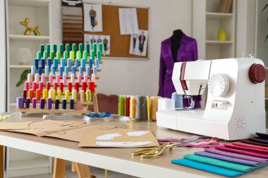 Atölyedeki terzi masasında iplik makaralı dikiş makinesi ve desenler