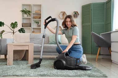 Oturma odasında halı süpürgesiyle gezen genç bir kadın.