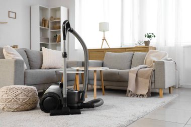 Elektrik süpürgesi, kanepe ve masalarla aydınlık oturma odasının içinde.