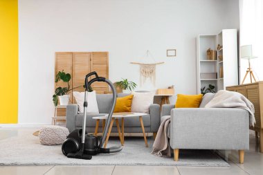 Elektrik süpürgesi, kanepe ve masalarla aydınlık oturma odasının içinde.