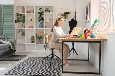 Atölyede dizüstü bilgisayarla çalışan kadın terzi.